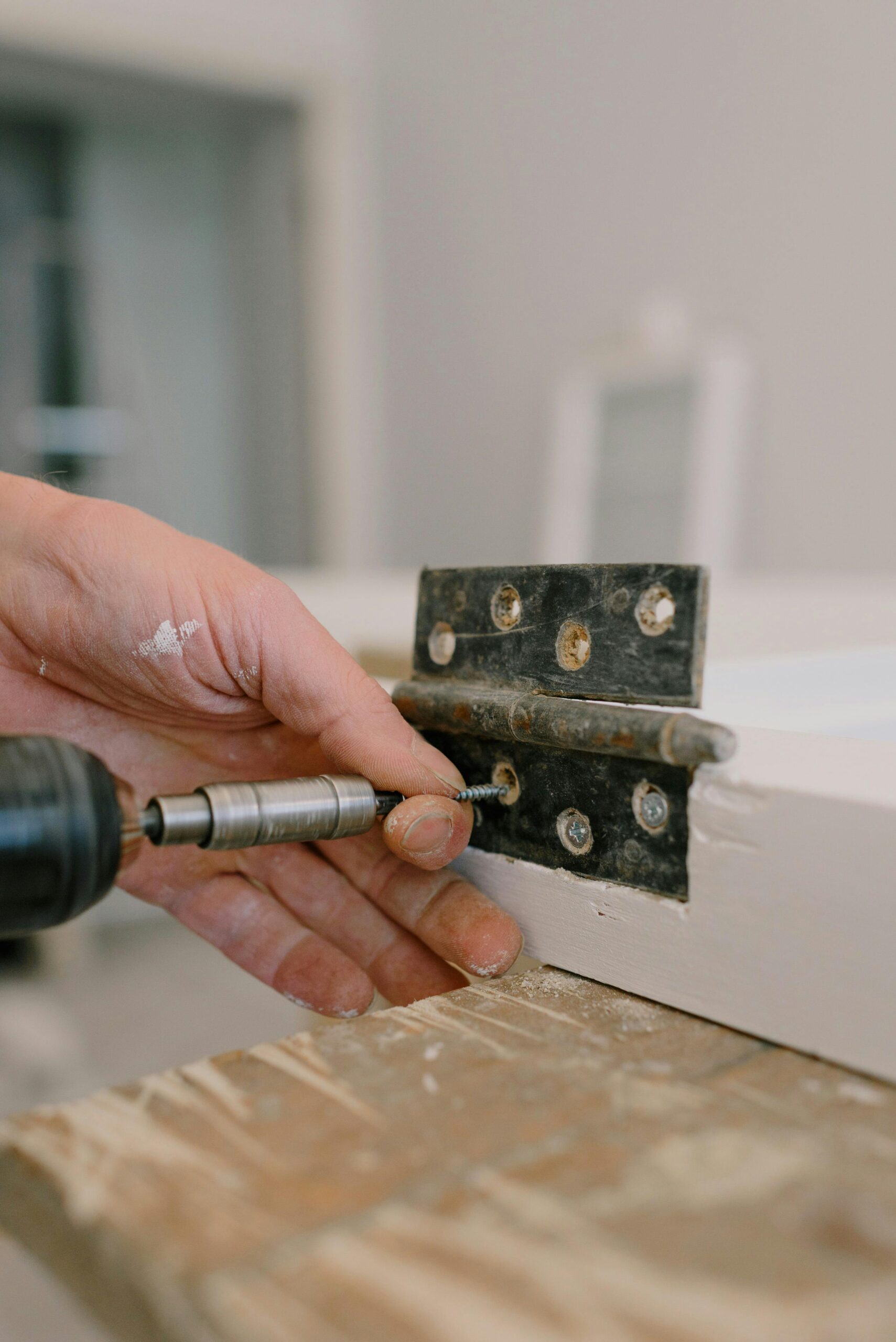 door fixing carpenter using screwdriver to attach metal hinge on window in room with blurred background during renovation works